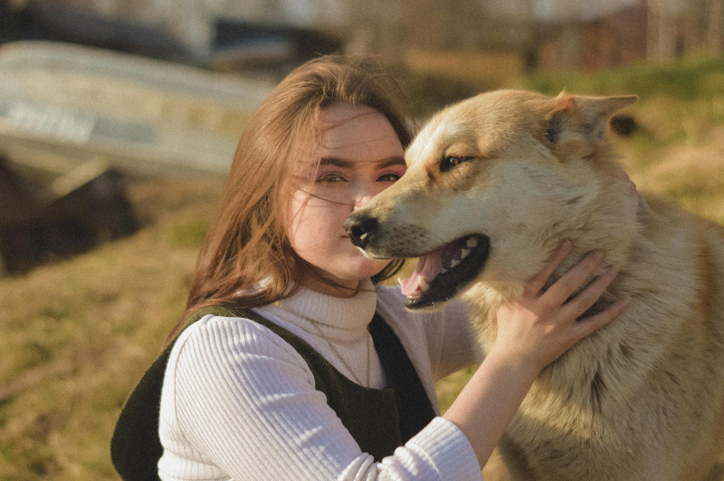 A woman joyfully embraces her happy dog in a sunny outdoor setting, conveying affection and companionship.